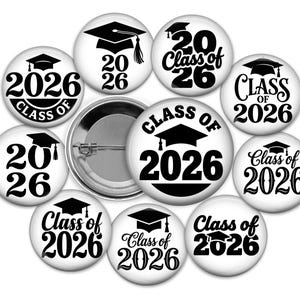May include: A collection of white graduation buttons with black text and graphics. Each button features the year "2026" and a graduation cap, with some also including "Class of 2026". A silver button back is also visible.