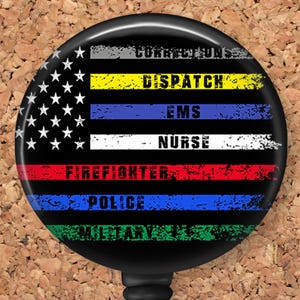 May include: A black and white American flag with thin colored stripes representing different professions. The stripes read "Corrections", "Dispatch", "EMS", "Nurse", "Firefighter", "Police", and "Military".