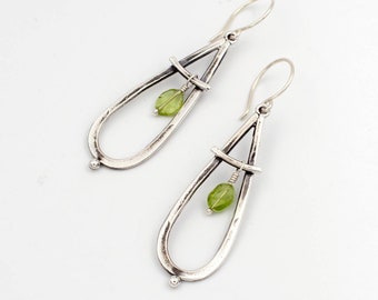 May include: Silver teardrop earrings with a geometric design and a green gemstone hanging from the bottom.