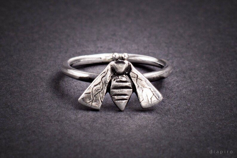 May include: A silver ring with a detailed bee design. The bee's wings are textured and the body is striped.