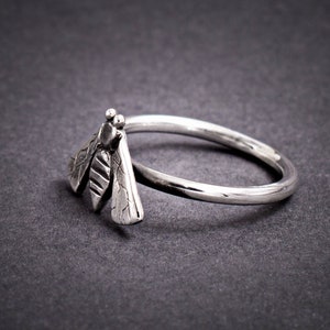 May include: A silver ring with a detailed dragonfly design. The dragonfly is facing to the right and has textured wings.