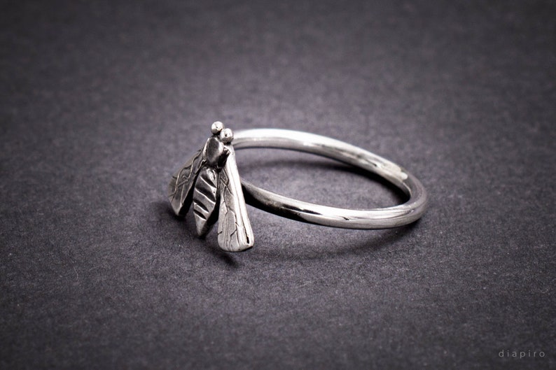 May include: A silver ring with a detailed dragonfly design. The dragonfly is facing to the right and has textured wings.