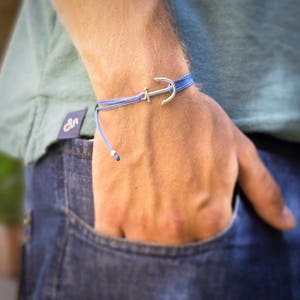 May include: A blue and silver anchor bracelet. The bracelet is made of a thin blue cord with a silver anchor charm.