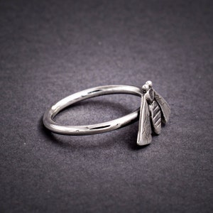 May include: A silver ring with a bee design. The bee is made of three separate pieces of metal, each with a textured surface.