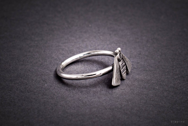 May include: A silver ring with a bee design. The bee is made of three separate pieces of metal, each with a textured surface.