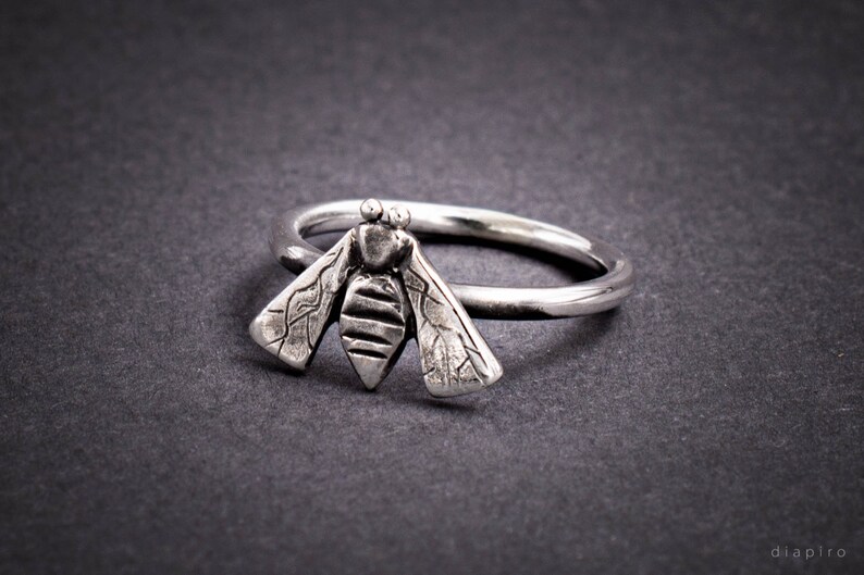 May include: A silver ring with a detailed bee design. The bee is textured and has wings that are spread out.