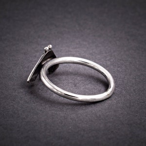 May include: A silver ring with a unique, abstract design. The ring is made of a single piece of metal that is bent and twisted to create a three-dimensional shape.