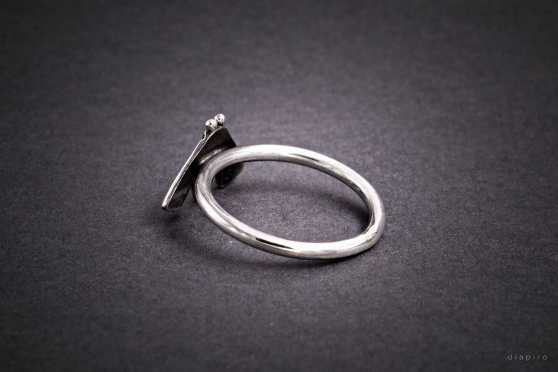 May include: A silver ring with a unique, abstract design. The ring is made of a single piece of metal that is bent and twisted to create a three-dimensional shape.