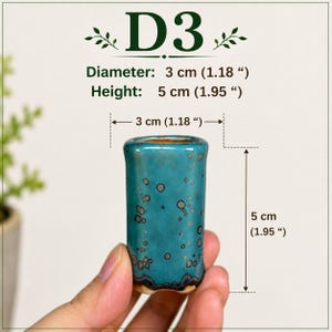 May include: A small cylindrical turquoise ceramic vessel with dark speckled patterns. Text D3 is displayed above with dimensions of 3 inches diameter and 5 inches height, though the actual object measures 3 cm in diameter and 5 cm in height.