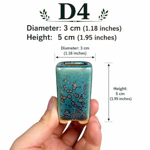May include: A small square ceramic pot with a teal and dark blue crystalline glaze. The pot is labeled D4 and measures 1.18 inches in diameter and 1.95 inches in height. The base is a light tan color, and the surface features a speckled pattern.