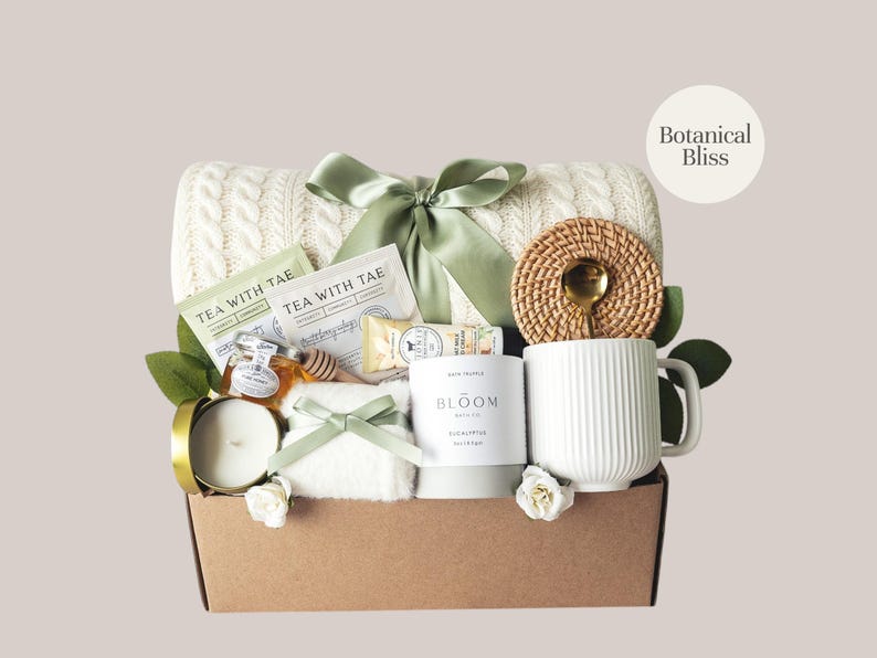 Peut inclure: Un panier cadeau rempli d'articles de bien-&ecirc;tre. Il comprend une couverture en tricot torsad&eacute; cr&egrave;me, des sachets de th&eacute;, du miel, une bougie, une tasse et un dessous de verre tress&eacute; avec une cuill&egrave;re dor&eacute;e. Le panier est nou&eacute; avec un ruban vert et contient le texte "Botanical Bliss".