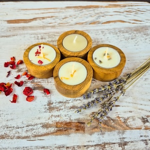 Peut inclure: Quatre bougeoirs en bois pour bougies chauffe-plat avec des bougies allum&eacute;es. Les bougies sont entour&eacute;es de p&eacute;tales de fleurs s&eacute;ch&eacute;es et de brins de lavande. Sur une surface en bois blanc vieilli.