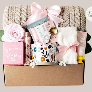 Peut inclure: Un panier cadeau rempli d'articles de bien-&ecirc;tre. Il comprend une bo&icirc;te de bombe de bain rose, une tasse &agrave; fleurs, du th&eacute;, une petite serviette nou&eacute;e avec un n&oelig;ud rose, une lotion &agrave; la rose et une rose rose. Le panier est doubl&eacute; d'une couverture en tricot de c&acirc;ble beige.