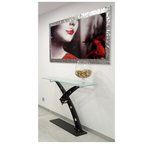 May include: A black metal console table with a glass top. The table has a unique X-shaped base with curved arms. A glass bowl filled with colorful candies sits on the table.