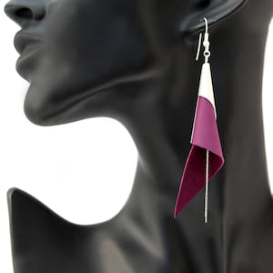 Puede incluir: Un par de pendientes colgantes con un gancho plateado y una forma de lágrima de cuero morado y blanco.