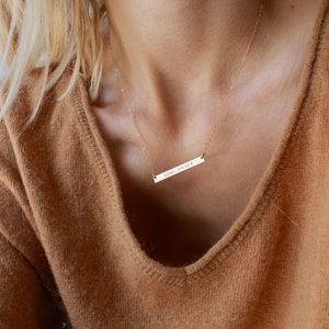 May include: A gold necklace with a thin chain and a horizontal bar pendant that says 'GIRL POWER'.
