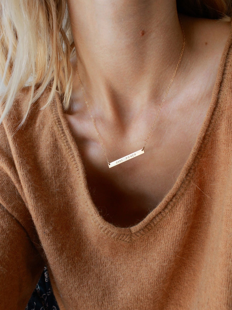 May include: A gold necklace with a thin chain and a horizontal bar pendant that says 'GIRL POWER'.