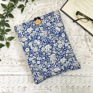May include: A blue floral book sleeve with a button fastening. The sleeve features a pattern of white flowers and foliage. A book and spectacles are visible in the background.