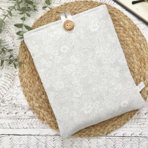 May include: A rectangular fabric pouch featuring a light grey and white floral pattern. The pouch is secured with a white fabric loop and a single round wooden button centred at the top edge. A small white fabric tag is visible on the right side.