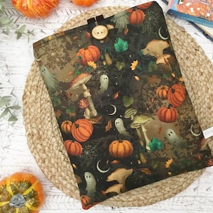 May include: A rectangular fabric pouch featuring a dark pattern of orange pumpkins, white ghosts, various mushrooms, and crescent moons. The pouch is secured at the top with a single wooden button and a dark fabric loop closure.
