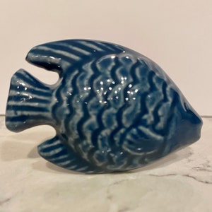 May include: A ceramic fish figurine in a deep blue hue. The fish has detailed scale patterns and fins, with a glossy finish. The figurine is a decorative item, likely for home decor or a nautical-themed collection.