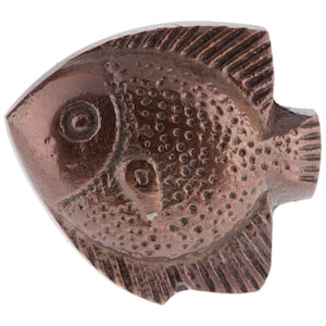 May include: A bronze-colored, fish-shaped cabinet knob. The knob features a detailed design with scales, fins, and an eye. The fish is oriented horizontally, with the head on the left and the tail on the right. The knob is made of a solid material.