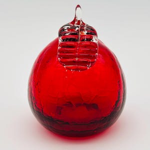May include: A vibrant red glass ornament with a textured surface and a clear, decorative top. The ornament has a round shape and is likely for holiday or seasonal decor.