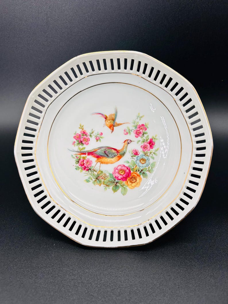 Peut inclure: Assiette en porcelaine blanche avec un bord dor&eacute; et un motif d&eacute;coratif d'oiseaux et de fleurs. L'assiette a un bord festonn&eacute; avec un motif d&eacute;coup&eacute;.