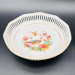 Peut inclure: Un bol en porcelaine blanche avec un bord dor&eacute; et un d&eacute;licat motif ajour&eacute; autour du bord. Le bol pr&eacute;sente un motif floral color&eacute; avec deux oiseaux au centre.