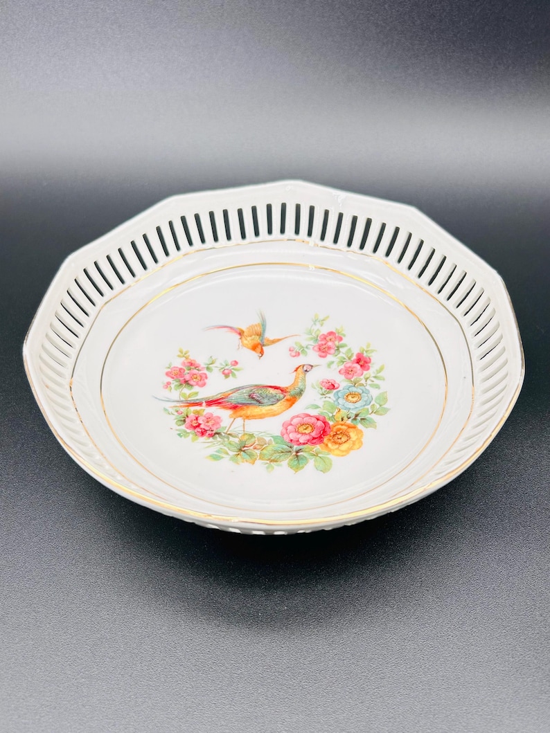 Peut inclure: Un bol en porcelaine blanche avec un bord dor&eacute; et un d&eacute;licat motif ajour&eacute; autour du bord. Le bol pr&eacute;sente un motif floral color&eacute; avec deux oiseaux au centre.