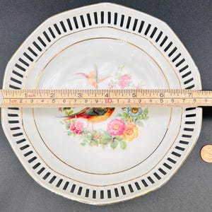 Peut inclure: Une assiette en porcelaine blanche avec un bord festonn&eacute; noir et blanc. Le centre de l'assiette pr&eacute;sente un bord dor&eacute; et un motif floral avec deux oiseaux. L'assiette mesure environ 20 cm de diam&egrave;tre.
