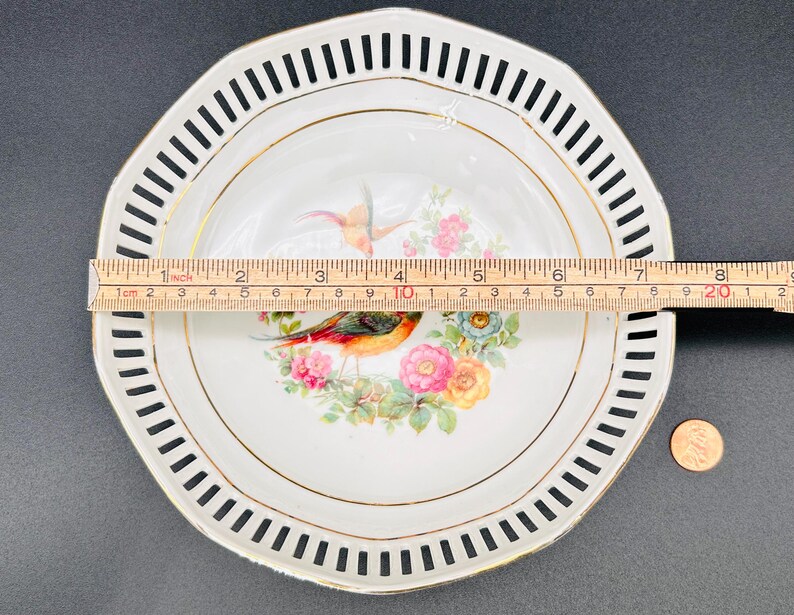Peut inclure: Une assiette en porcelaine blanche avec un bord festonn&eacute; noir et blanc. Le centre de l'assiette pr&eacute;sente un bord dor&eacute; et un motif floral avec deux oiseaux. L'assiette mesure environ 20 cm de diam&egrave;tre.