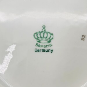 Peut inclure: Un gros plan d'une assiette en porcelaine blanche avec une couronne verte et les mots "Bavaria Germany" imprim&eacute;s au bas. Le num&eacute;ro "92" est &eacute;galement imprim&eacute; sur l'assiette.