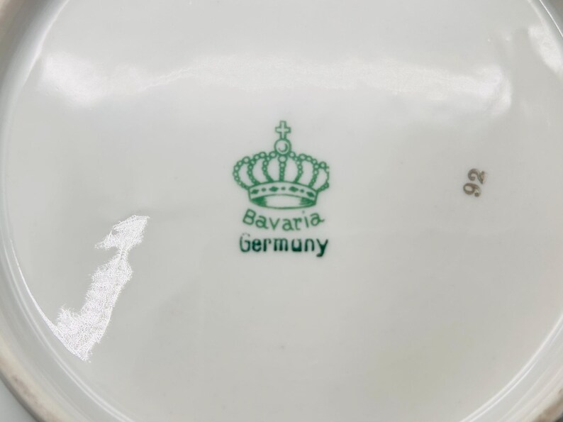 Peut inclure: Un gros plan d'une assiette en porcelaine blanche avec une couronne verte et les mots "Bavaria Germany" imprim&eacute;s au bas. Le num&eacute;ro "92" est &eacute;galement imprim&eacute; sur l'assiette.