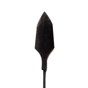 Op de afbeelding: Een donkere, houten speerpunt met een puntige punt en een slanke, langwerpige schacht. De speerpunt heeft een diepe, rijke zwarte kleur en de houtnerf is zichtbaar. Op een effen witte achtergrond.