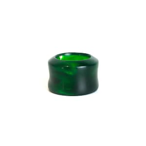Puede incluir: Un objeto cilíndrico verde oscuro con una forma curva y orgánica. El objeto tiene un centro hueco y un acabado brillante, con veteado visible. El producto está sobre un fondo blanco.