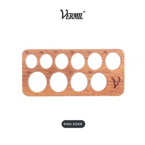 Puede incluir: Un medidor de anillos rectangular de madera con el nombre de la marca Vermil en la parte superior y el texto Ring Sizer en la parte inferior. La herramienta contiene diez aberturas circulares de varios tamaños, numeradas del 15 al 24, y un logo V estilizado.