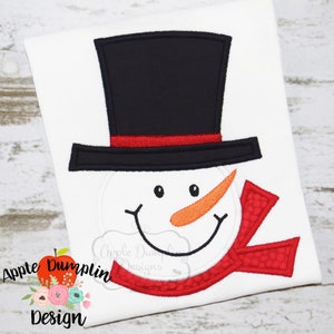May include: Embroidered snowman face with a black top hat, red scarf, and orange nose. The design is perfect for a holiday craft project.