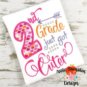 May include: A pink and orange embroidered design on a white t-shirt that says "2nd grade just got cuter". The number 2 is decorated with pink and orange mermaid scales.