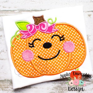 May include: Embroidered pumpkin with a pink bow and a smiling face. The pumpkin is orange with white polka dots and pink cheeks.