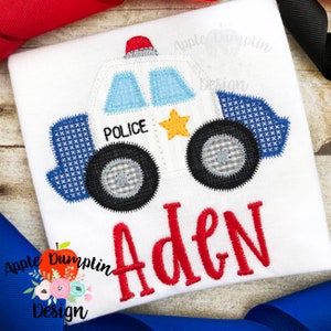 May include: A white and blue police car applique with a yellow star and the word "POLICE" on the side. The name "Aden" is embroidered in red below the car.