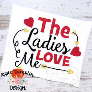 May include: Embroidered design on a white t-shirt that reads "The Ladies Love Me" with red hearts and gold arrows. The design is by Apple Dumplin Design.