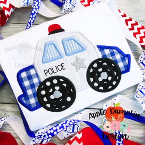 May include: White police car applique with blue and white checkered trim, black wheels with white polka dots, and the word "POLICE" on the side.