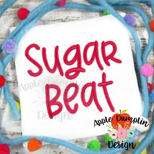 May include: White square-shaped fabric with the words "Sugar Beat" embroidered in red cursive. The design is surrounded by a blue garland with colorful pom-poms. The Apple Dumplin Design logo is in the bottom right corner.