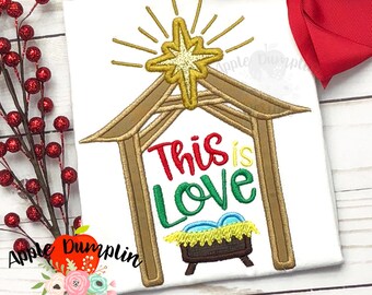 May include: Embroidered design of a manger scene with a star above it and the text "This is Love". The manger is brown, the star is gold, and the text is red, green, and blue.