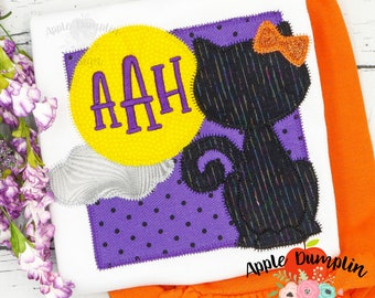 Puede incluir: Un pelele blanco con un diseño de aplique morado, amarillo y negro que presenta un gato negro, una luna amarilla con las letras "AAH" en ella y un fondo morado con lunares blancos.