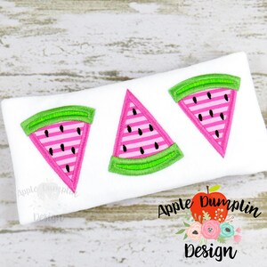 May include: Three watermelon slices embroidered on a white fabric. The watermelon slices are pink with black seeds and green outlines.