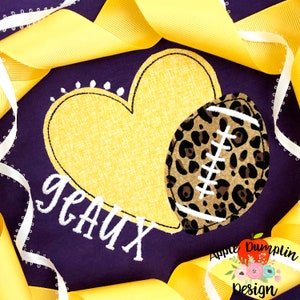 May include: Purple fabric with a yellow heart and a brown and white football with a leopard print design. The text "geaux" is embroidered in white below the heart.