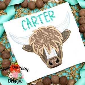 Op de afbeelding: Wit geborduurd T-shirt met een bruin en wit Highland-koeienkopontwerp en de naam "CARTER" in turquoise letters.