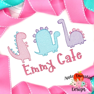 May include: Embroidered design featuring three dinosaurs in pink, blue, and purple, with the name "Emmy Gale" stitched below. The design is on a white background.